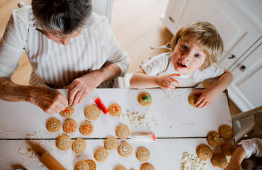 Draufsicht auf eine ältere Großmutter mit einem kleinen Jungen im Kleinkindalter, die zu Hause Kuchen backen und verzieren. - HPIF23616