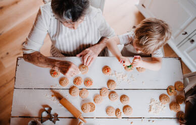 Draufsicht auf eine ältere Großmutter mit einem kleinen Jungen im Kleinkindalter, die zu Hause Kuchen backen und verzieren. - HPIF23617