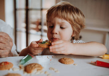 Ein kleines glückliches Kleinkind, das zu Hause am Tisch sitzt und Kuchen dekoriert und isst. - HPIF23619