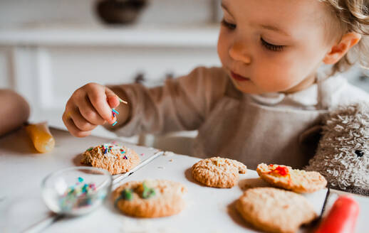 Ein glückliches kleines Mädchen sitzt am Tisch und dekoriert zu Hause Kuchen. - HPIF23621