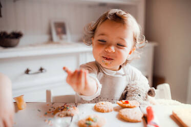 Ein glückliches kleines Mädchen sitzt am Tisch und dekoriert zu Hause Kuchen. - HPIF23624