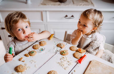 Zwei glückliche Kleinkinder, die zu Hause am Tisch sitzen und Kuchen dekorieren und essen. - HPIF23626