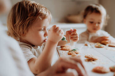 Zwei glückliche Kleinkinder, die zu Hause am Tisch sitzen und Kuchen dekorieren und essen. - HPIF23628