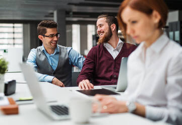 A group of young businesspeople with laptop working together in office, talking. - HPIF23656