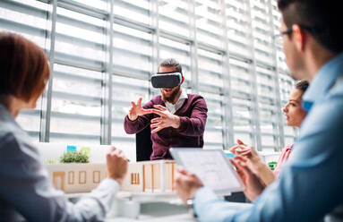 A group of young architects with model of a house and VR goggles working in office, talking. - HPIF23663