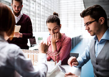 Eine Gruppe junger Architekten mit dem Modell eines Hauses steht in einem Büro, arbeitet und unterhält sich. - HPIF23664