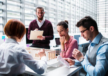 A group of young architects with model of a house working in office, talking. - HPIF23665