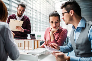 Eine Gruppe junger Architekten mit dem Modell eines Hauses steht in einem Büro, arbeitet und unterhält sich. - HPIF23666