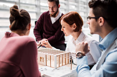 Eine Gruppe junger Architekten mit dem Modell eines Hauses steht in einem Büro, arbeitet und unterhält sich. - HPIF23669