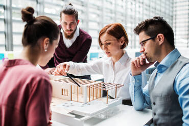 A group of young architects with model of a house working in office, talking. - HPIF23670