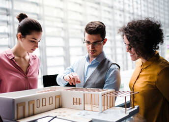 Eine Gruppe junger Architekten mit dem Modell eines Hauses steht in einem Büro, arbeitet und unterhält sich. - HPIF23677