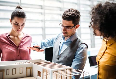 Eine Gruppe junger Architekten mit dem Modell eines Hauses steht in einem Büro, arbeitet und unterhält sich. - HPIF23678