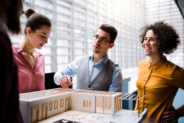 Eine Gruppe junger Architekten mit dem Modell eines Hauses steht in einem Büro, arbeitet und unterhält sich. - HPIF23679