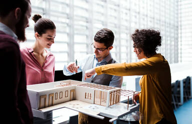 Eine Gruppe junger Architekten mit dem Modell eines Hauses steht in einem Büro, arbeitet und unterhält sich. - HPIF23680