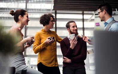 Eine Gruppe fröhlicher junger Geschäftsleute steht mit einer Tasse Kaffee im Büro und unterhält sich. - HPIF23686
