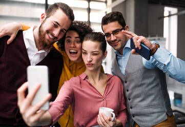 Eine Gruppe junger Berufstätiger im Büro, die einen glücklichen Moment mit einem Selfie auf ihren Smartphones festhalten - HPIF23693