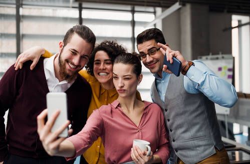 Eine Gruppe junger Berufstätiger im Büro, die einen glücklichen Moment mit einem Selfie auf ihren Smartphones festhalten - HPIF23694