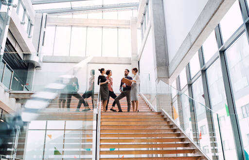 A group of young businesspeople standing on a staircase, talking. - HPIF23697