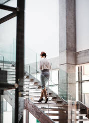 Rückansicht einer jungen Geschäftsfrau, die in einem Bürogebäude die Treppe hinaufgeht. Raum kopieren. - HPIF23708