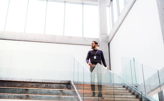 Ein junger Geschäftsmann, der in einem Bürogebäude die Treppe hinuntergeht. Raum kopieren. - HPIF23710