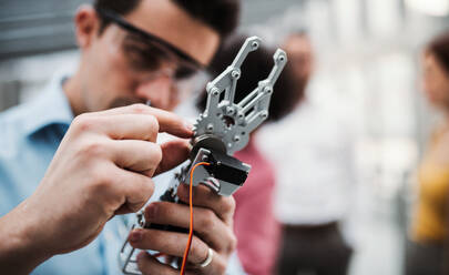 A young businessman or scientist with robotic hand and safety glasses standing in office, working. - HPIF23718