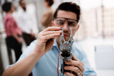 Ein junger Geschäftsmann oder Wissenschaftler mit Roboterhand und Schutzbrille steht im Büro und arbeitet. - HPIF23719