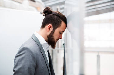 Ein trauriger und frustrierter junger Geschäftsmann im Anzug steht im Büro und stützt sich mit dem Kopf gegen die Wand. - HPIF23726