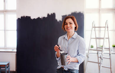 A portrait of young creative woman painting wall black. A startup of small business. - HPIF23727