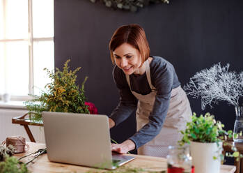 Eine junge kreative Frau arrangiert Blumen in einem Blumenladen mit einem Laptop. - HPIF23752