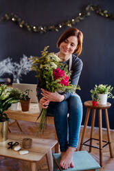 Eine junge, kreative Frau, die in einem Blumenladen Blumen arrangiert, eine Neugründung eines Blumenladens. - HPIF23756