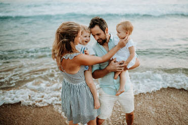 Eine glückliche junge Familie mit zwei Kleinkindern steht im Sommerurlaub am Strand. - HPIF23769