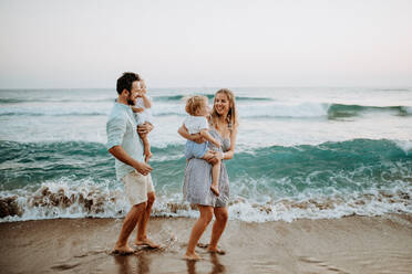 Eine junge Familie mit zwei Kleinkindern geht im Sommerurlaub am Strand spazieren. - HPIF23770