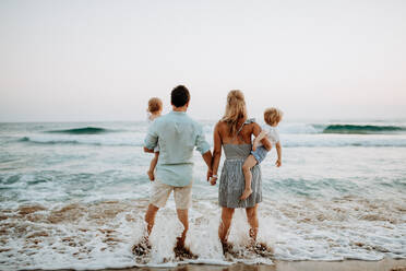 Rückansicht einer jungen Familie mit zwei Kleinkindern, die im Sommerurlaub am Strand stehen. - HPIF23771