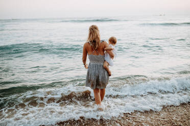 A rear view of young mother with a toddler girl walking in sea on summer holiday. - HPIF23778