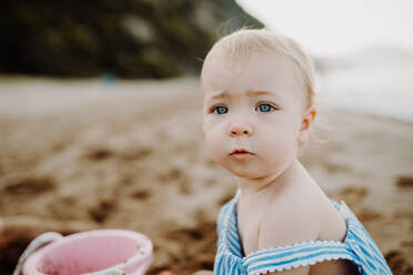 A close-up of small toddler girl on beach on summer holiday, playing. Copy space. - HPIF23785