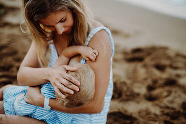 Eine junge Mutter stillt ihre kleine Tochter am Strand im Sommerurlaub. - HPIF23790