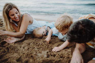 A family with two toddler children lying on sand beach on summer holiday, playing. - HPIF23792