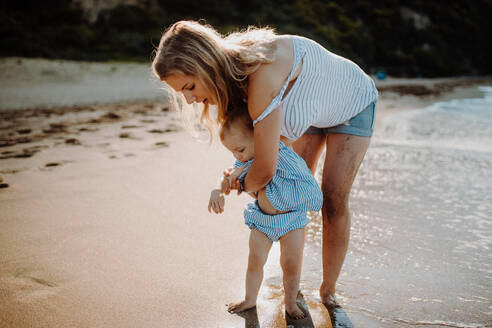 A young mother with small toddler daughter walking on beach on summer holiday. - HPIF23797