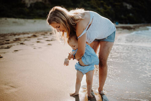 Eine junge Mutter mit ihrer kleinen Tochter geht im Sommerurlaub am Strand spazieren. - HPIF23797