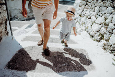 A midsection of unrecoognizable father with toddler son walking in town on summer holiday. - HPIF23801