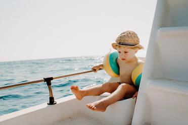 Ein kleiner Junge mit Armbinden sitzt im Sommerurlaub auf einem Boot und hält sich an einer Reling fest. - HPIF23804