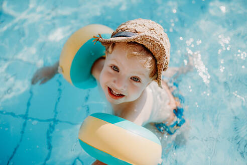 Ein glücklicher kleiner Junge mit Armbändern, der im Sommerurlaub im Wasser schwimmt. - HPIF23808