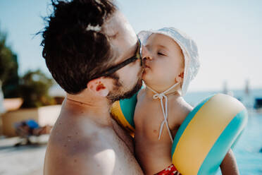 Ein Vater mit einem kleinen Kind mit Armbändern steht am Swimmingpool im Sommerurlaub. - HPIF23810