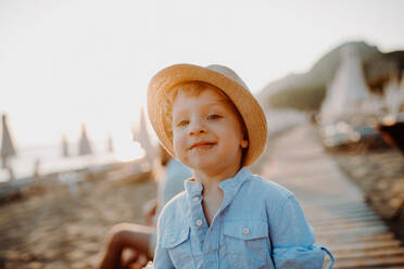 Ein kleiner Junge mit Hut steht am Strand im Sommerurlaub bei Sonnenuntergang. - HPIF23813