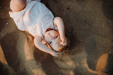 Eine Draufsicht auf ein kleines Kleinkind, das im Sommerurlaub am Strand im Sand spielt und in die Kamera schaut. - HPIF23819