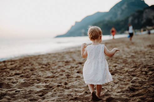 Rückansicht eines kleinen Mädchens, das im Sommerurlaub am Sandstrand spazieren geht, Kopierraum. - HPIF23825