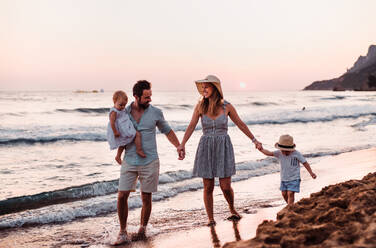 Eine junge Familie mit zwei Kleinkindern geht im Sommerurlaub am Strand spazieren. - HPIF23829