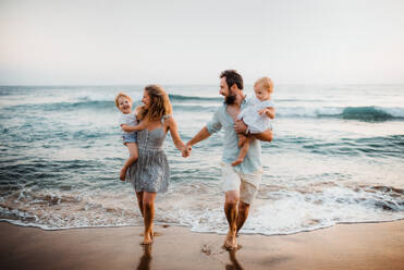 Eine junge Familie mit zwei Kleinkindern geht im Sommerurlaub am Strand spazieren. - HPIF23837
