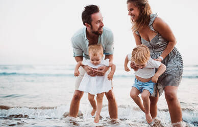 Eine junge Familie mit zwei Kleinkindern steht im Sommerurlaub am Strand und hat Spaß. - HPIF23841