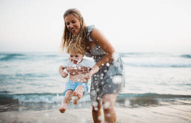 A young mother with a toddler boy standing on beach on summer holiday, having fun. - HPIF23842